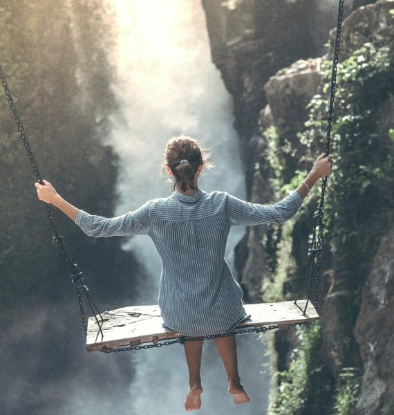 woman riding on wooden swing near waterfall