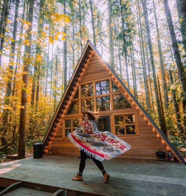 woman wearing blanket on shoulders walking in front of triangular house